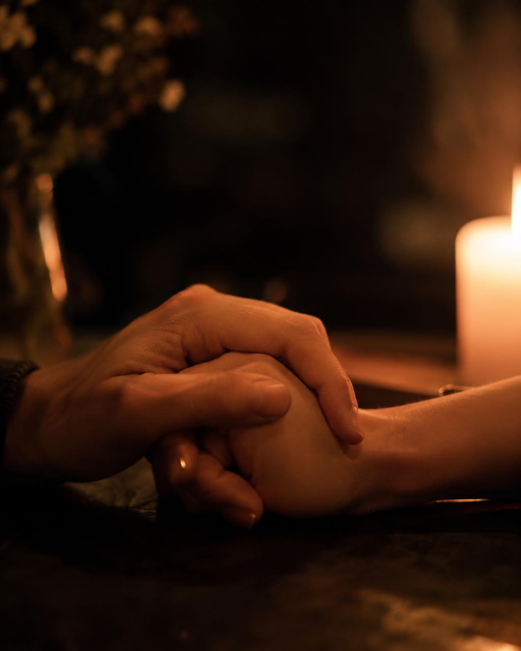 Two hands intertwined in candlelight